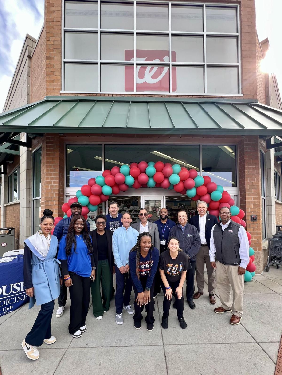 A group of people posed outside a Walgreens. A balloon arch over the entrance.