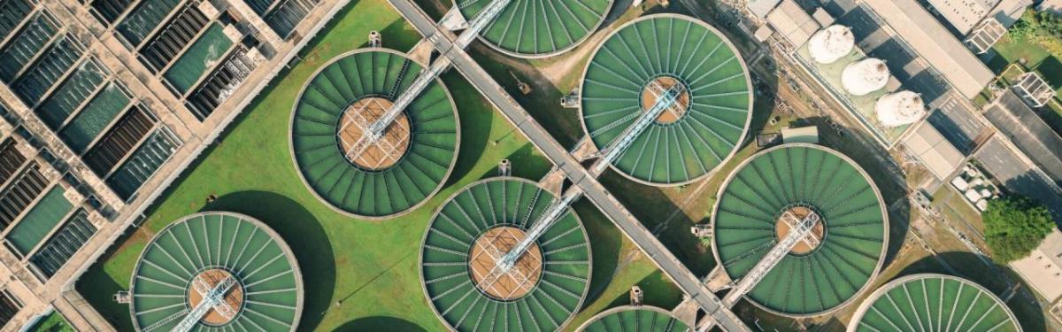 Aerial view of a large treatment plant with many open holding tanks with green substance. 