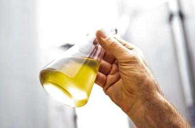 A hand holding a beaker of yellow liquid