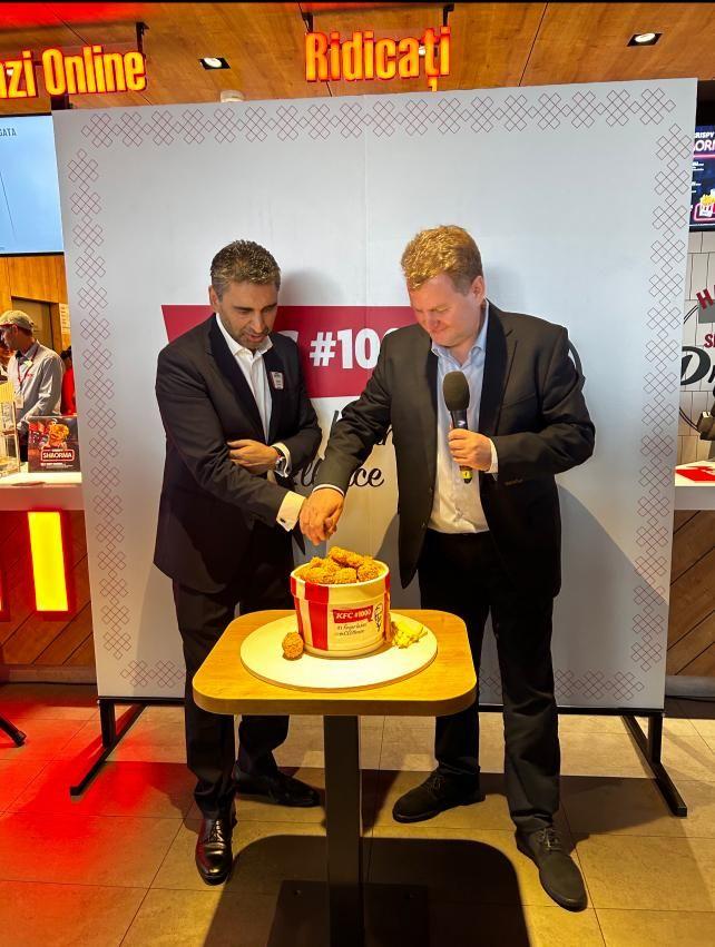 Two people cutting a cake in the shape of a KFC bucket of chicken.
