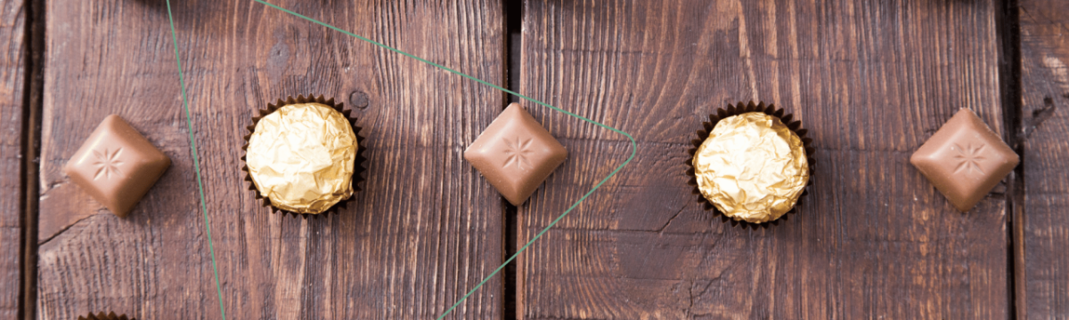 A row of five chocolates on a wood surface.