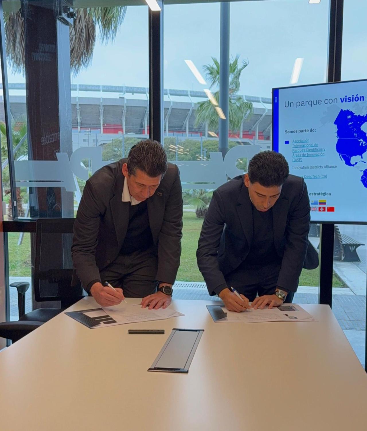 Two people signing a paper on a desk in front of a big window
