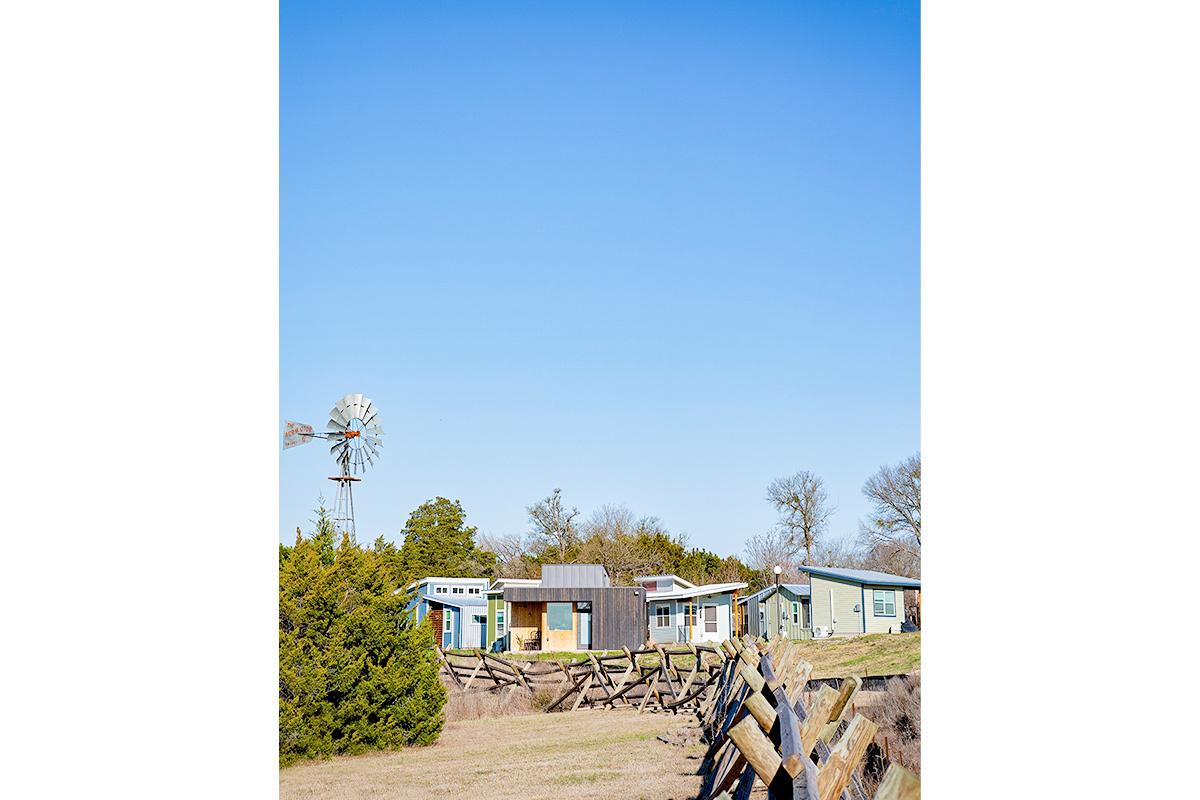 A fence line leading to a group of tiny homes. An old wind vane next to them.