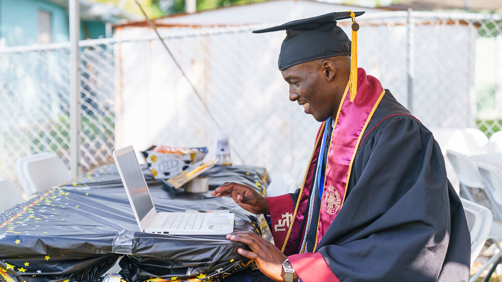 Man working on laptop in cap and gown