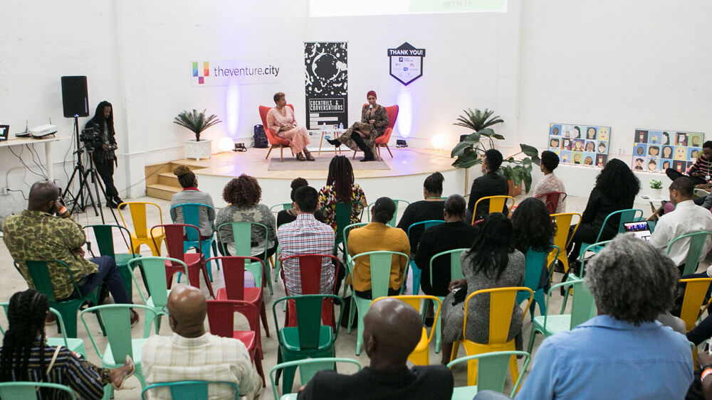 two people speak on stage with audience seated below