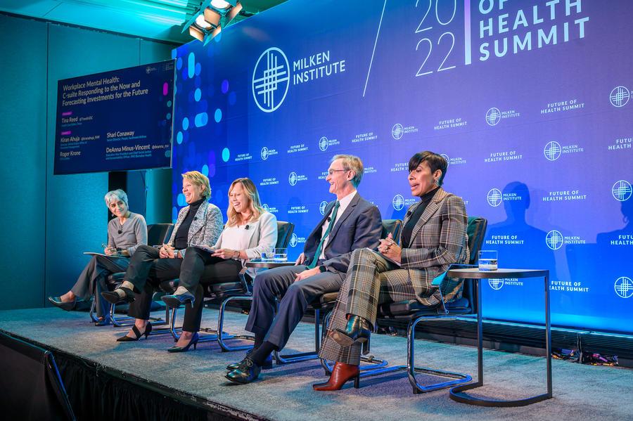Five people seated on a small stage. A large display behind them "2022 Future of Health Summit" and Milken Institute logos.