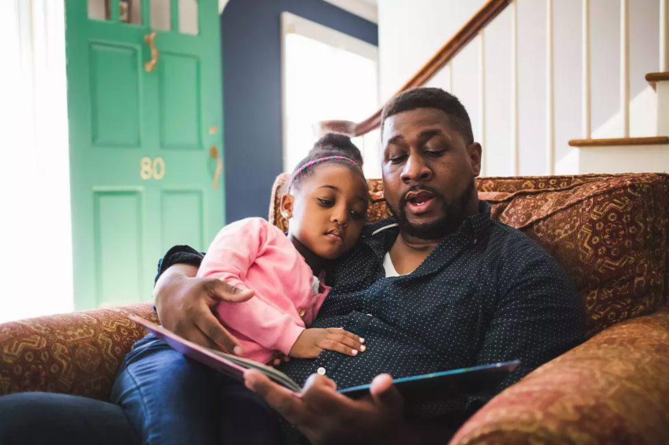 Father reading a book with daughter on couch