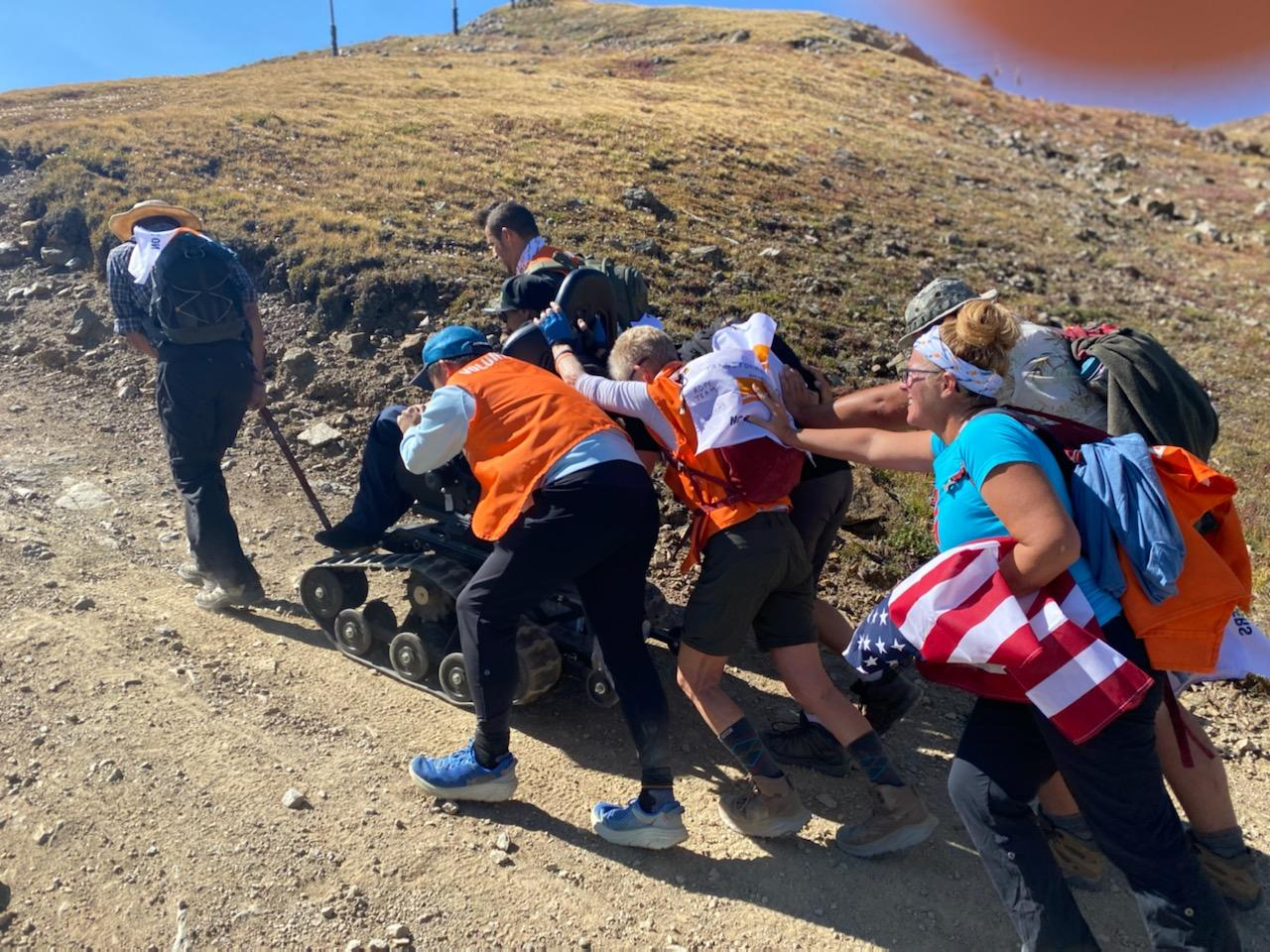 Hikers push a wheel chair up hill