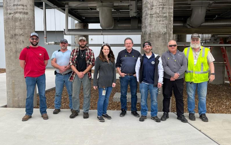 Eight people stand in a row outside . Large cement pillars behind them