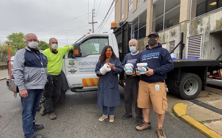 5 masked employees hold sanitizing wipes while standing in front of a truck. 