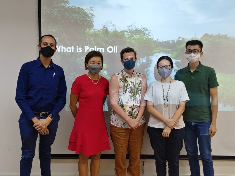 a group of 5 people stands in front of a screen with "what is palm oil" projected on it