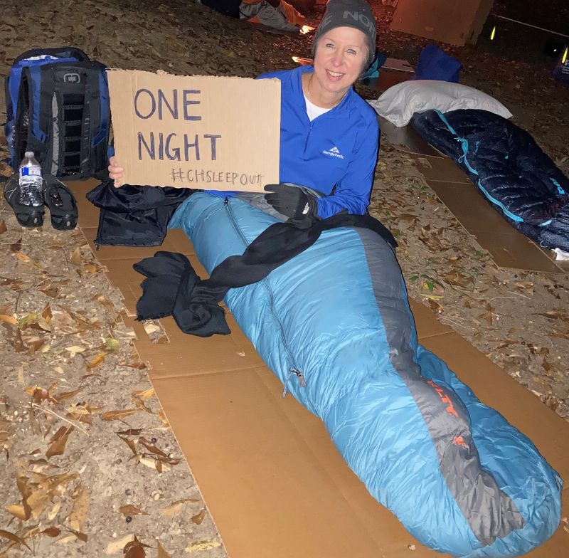 Woman in sleeping bag holding a cardboard sign that reads: One Night #CHSLEEPOUT