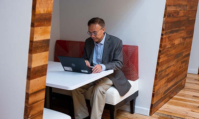 Zhang working on a laptop at a booth seat