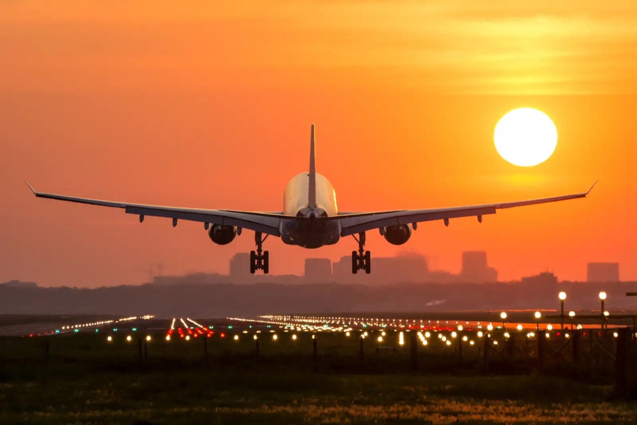 The back of a commercial jet as it takes off towards a setting sun