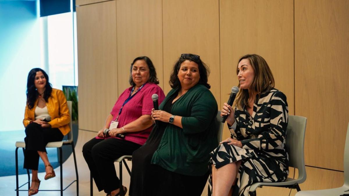 Four people seated at the front of a room, speaking with microphones.