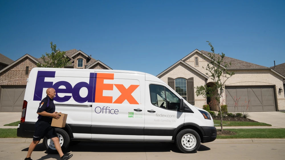 A delivery person walking with a package in a suburb, a FedEx transit van.