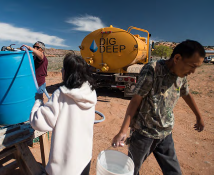 People filling buckets from a large blue container. A tank to the right with "Dig Deep" on the side.