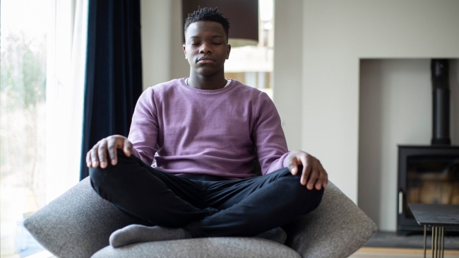 A black teen meditates on a chair