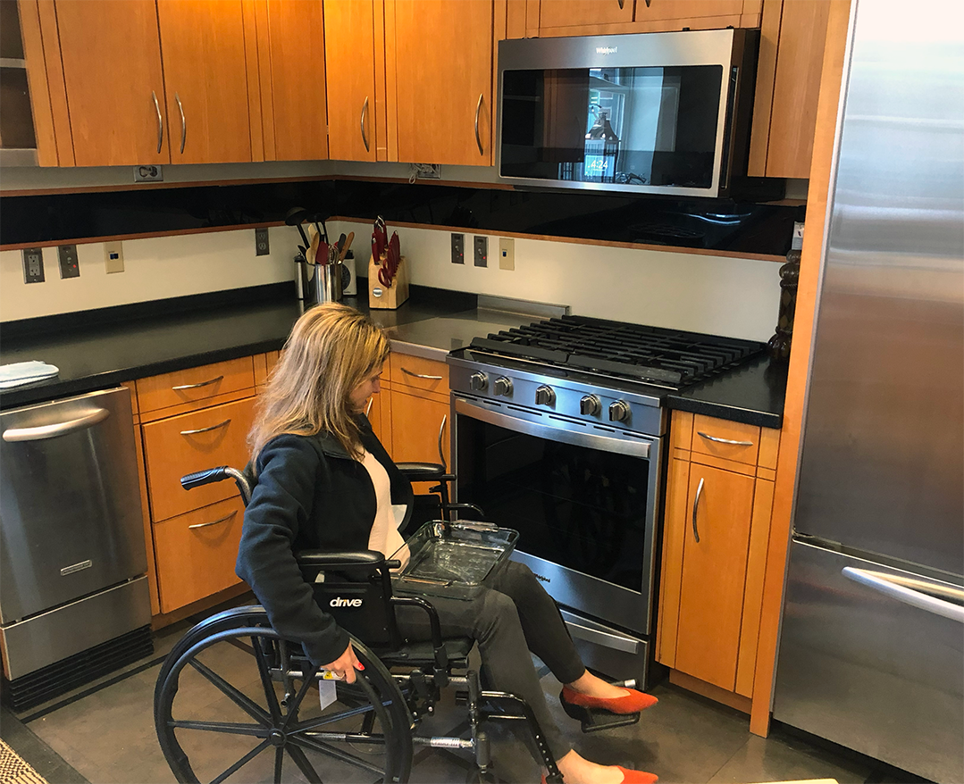 woman in a wheelchair approaching an oven with a glass casserole dish on her lap