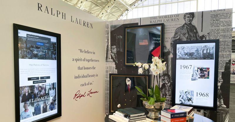 A display of "Ralph Lauren". Digital screens on the walls and a staged desk.