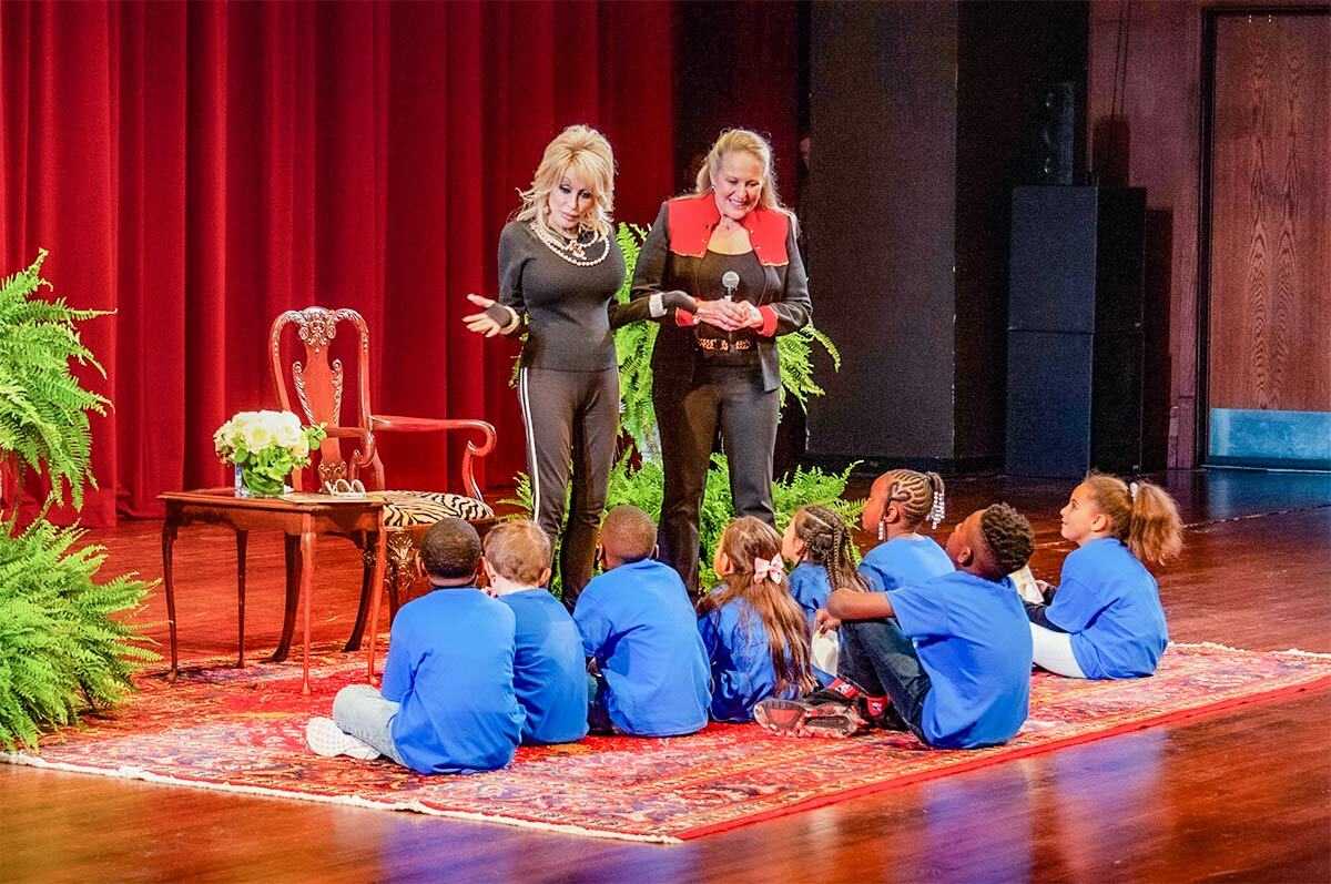 Dolly Parton on stage with another presenter, talking to a group of kids