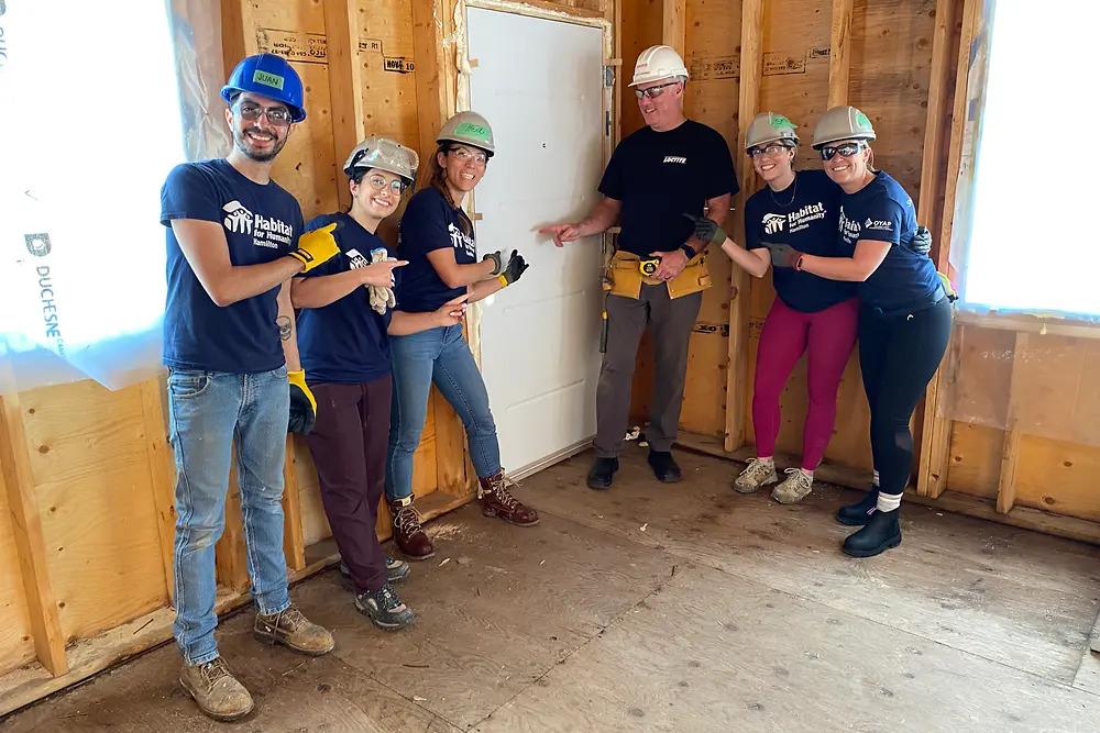 volunteers posed inside a home being built, pointing to the door.