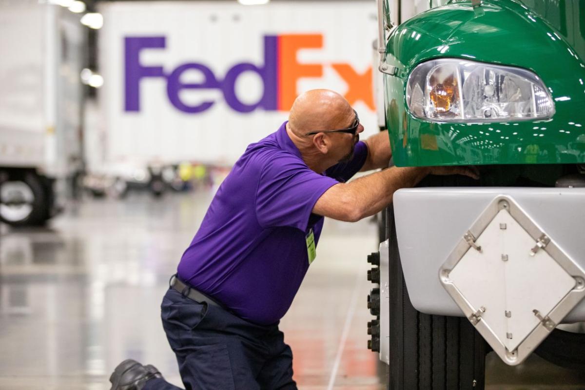 driver in purple shirt inspecting a green truck