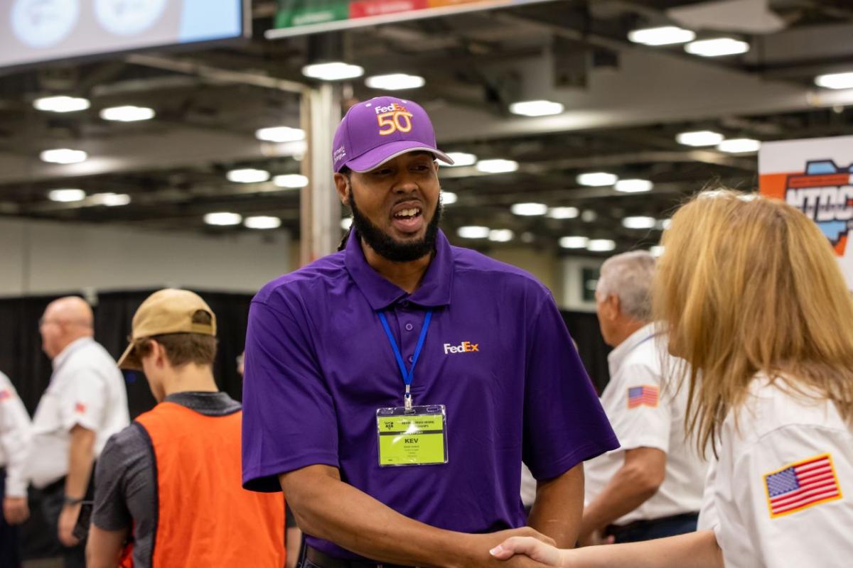 fedex driver in a purple hat shaking the hand of a competition judge
