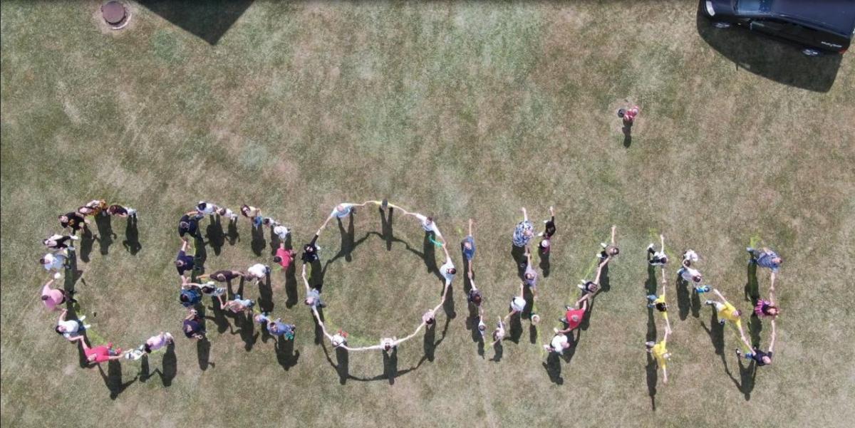 Aerial drone image of people in a field connected to form the word "CROWN".