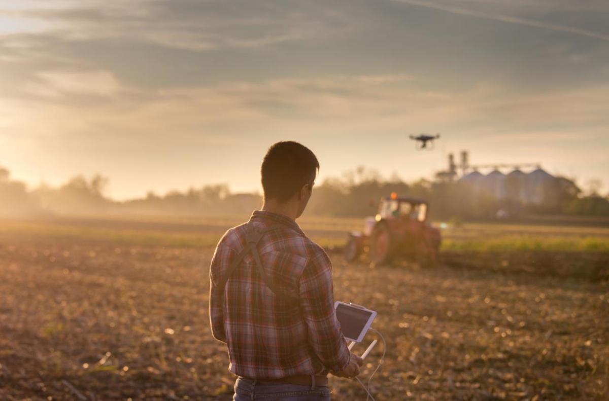 A farmer using a controller to fly a drone over farm fields.