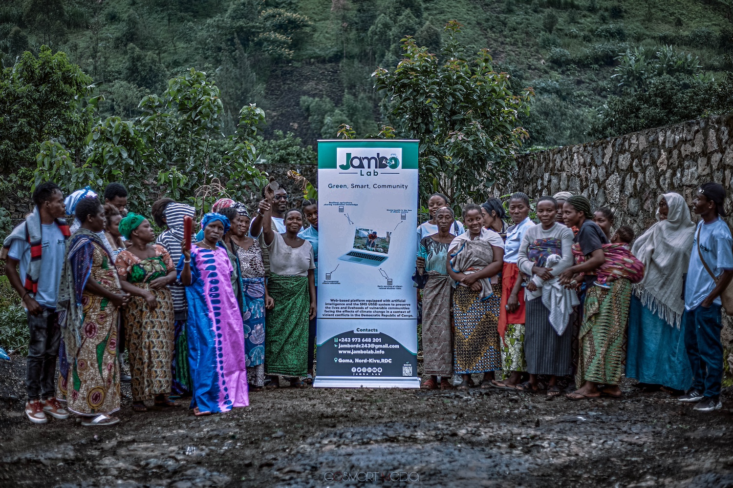 A group of community members smile at the camera alongside a Jambo Lab sign at an awareness session — early warning systems