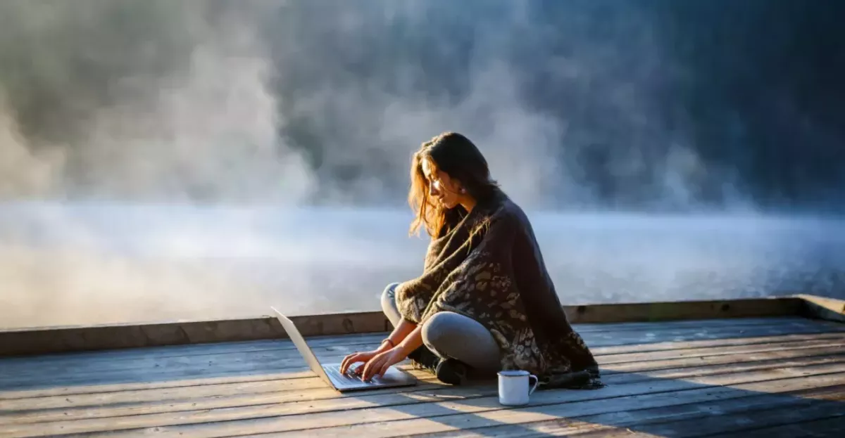 Woman sitting on a foggy dock with a laptop and cup of coffee