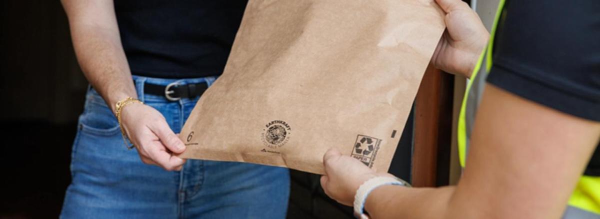 A person handing another a package in a brown Earth Kraft bag.