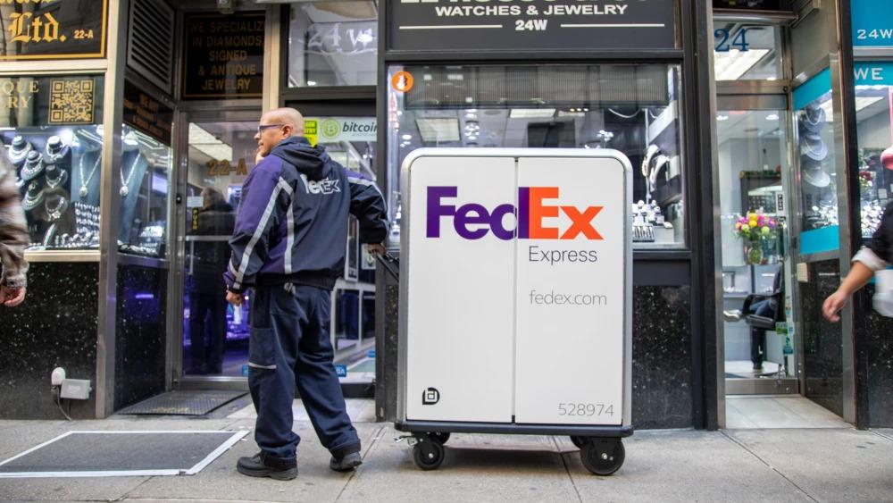 A person in FedEx uniform pulling a tall cart with FedEx Express logo on it, waiting outside of a jewelry store.