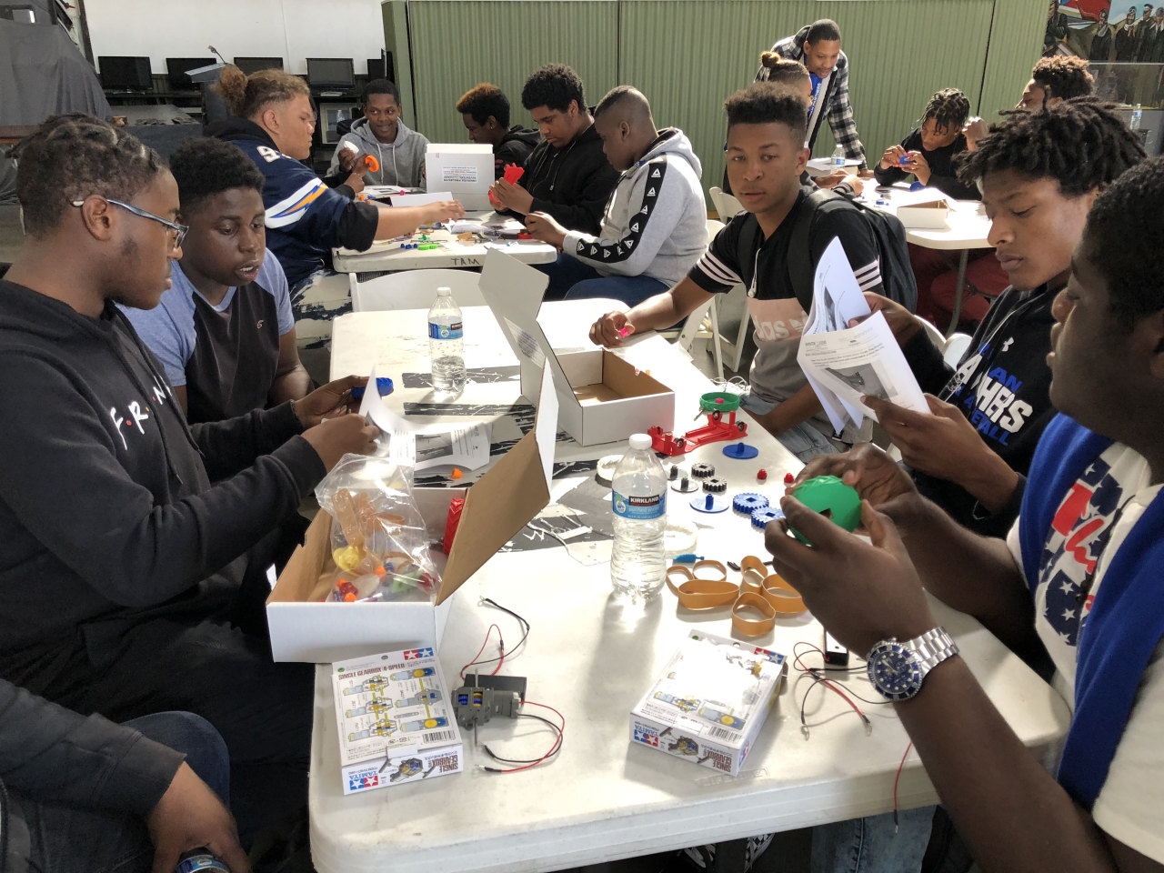 Students sit at a table assembling pieces of electronic equipment