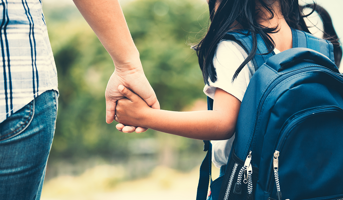 child wearing a backpack holding a grownup's hand