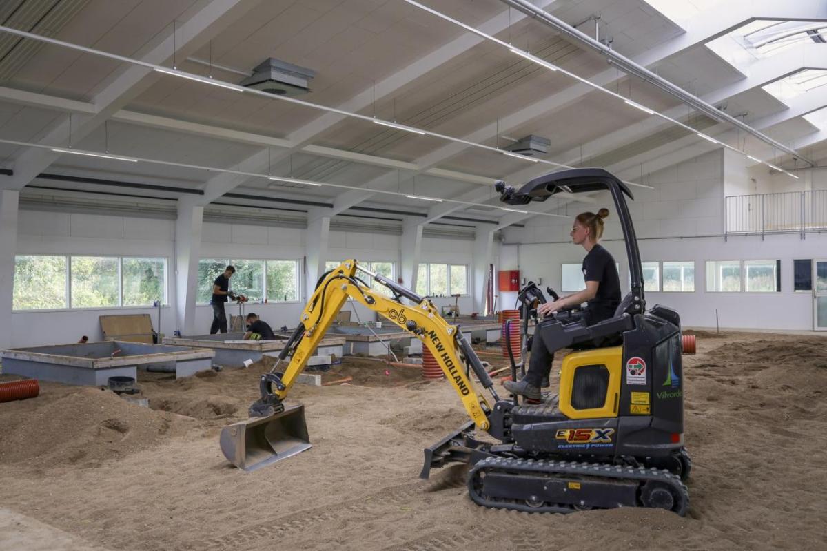 A person driving a digging machine in an enclosed sandy area.