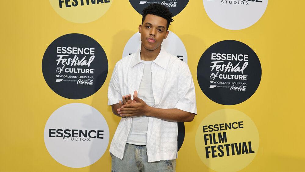 A person standing, facing the camera in front of a yellow backdrop with Essence Film Festival logos.