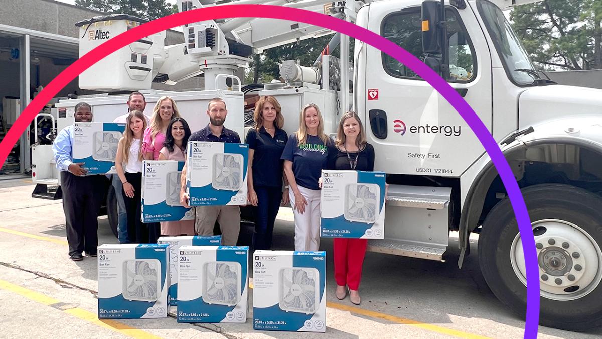 People posed outside with boxed fans in front of an Entergy bucket Truck.