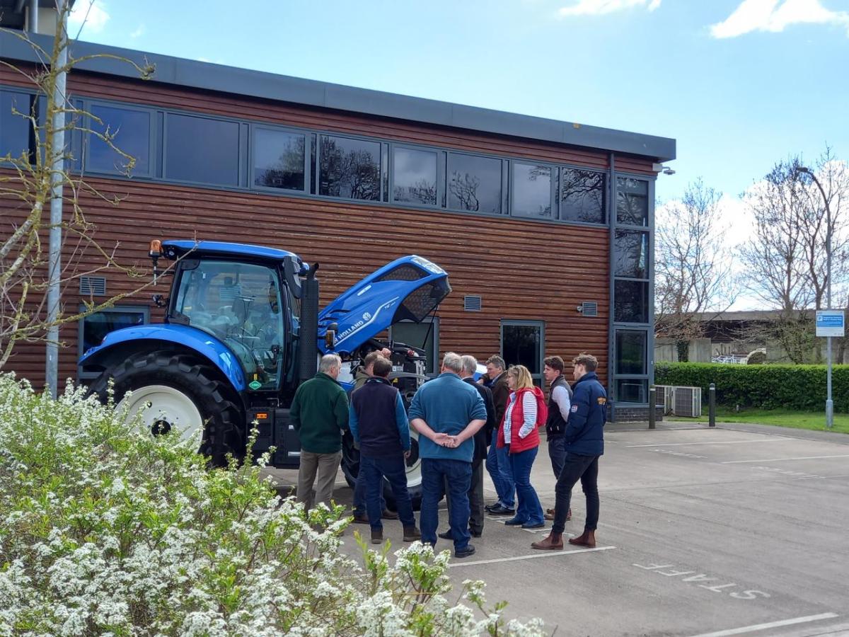 A small group of people gathered around a New Holland tractor in a parking lot.