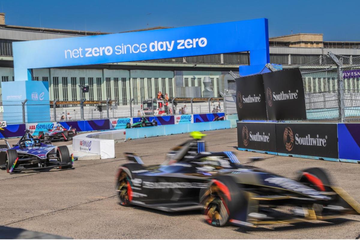 "Net zero since day zero" banner over a race track with cars going by.