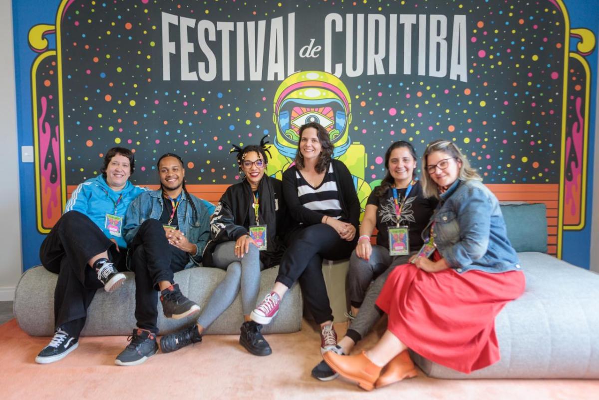 People seated on cushions, a large "Festival de Curitiba" sign behind them.