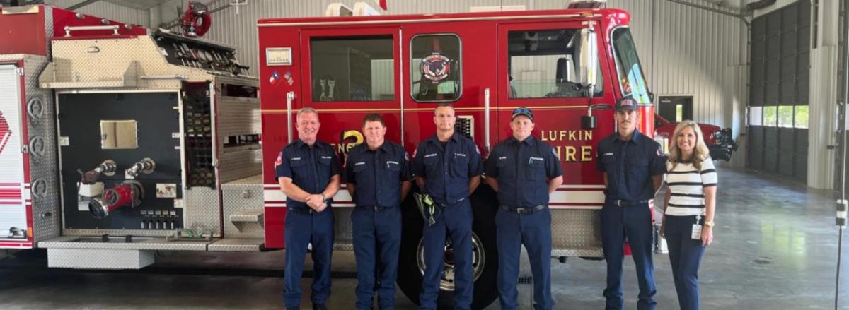 A row of people, some in uniform, in front of a fire truck.