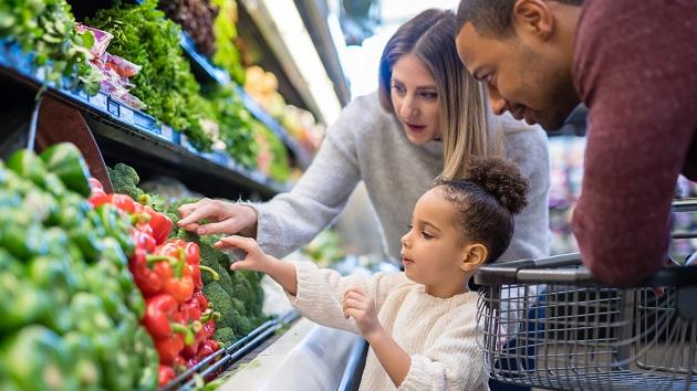 Two adults and a child looking at fresh vegetables in a grocery store.