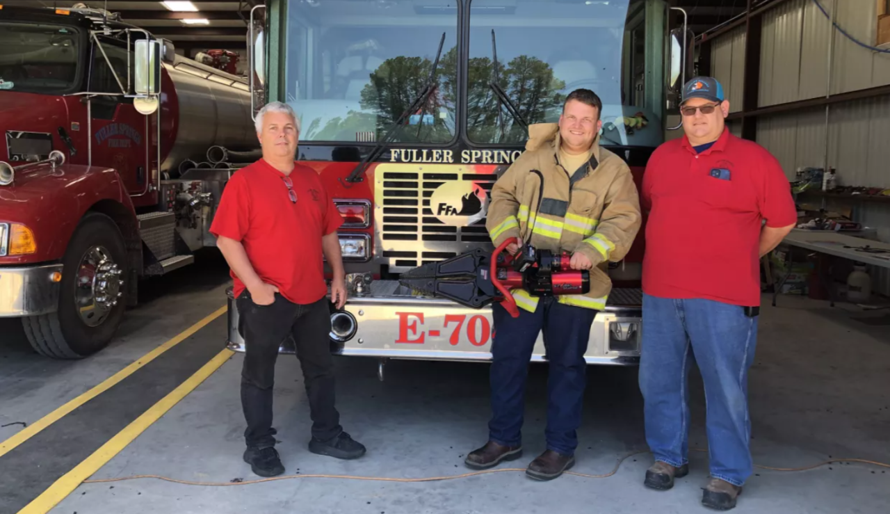 three people standing in front of a fire truck. One holding a 'jaws of life'.