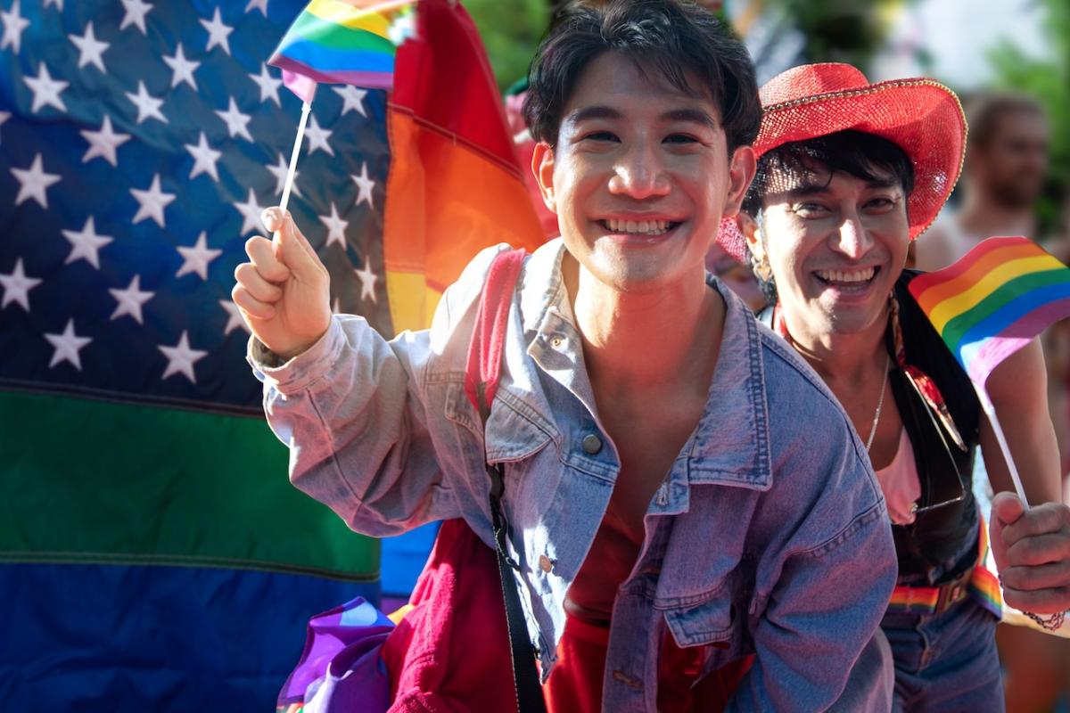 Young couple holding a rainbow flag in front of the US flag.