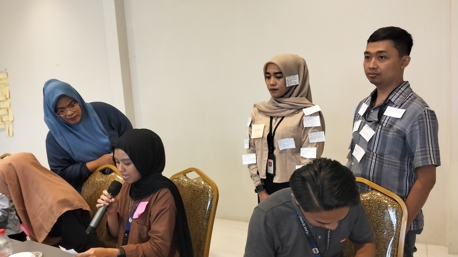 People partake in an educational exercise at a training session that involves attaching notes to the clothing of other participants — gender justice agreement