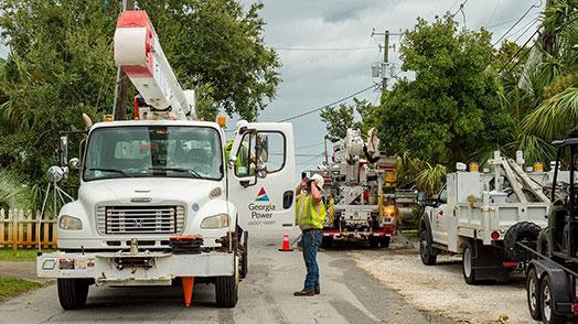 A person on a road talking to another inside a bucket truck with "Georgia Power" on the side. Other trucks on the road.