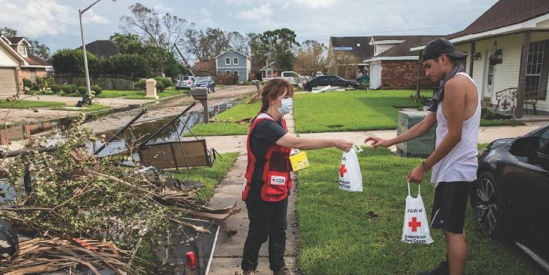 an american red cross volunteer handing a bag to another person, debris on the ground