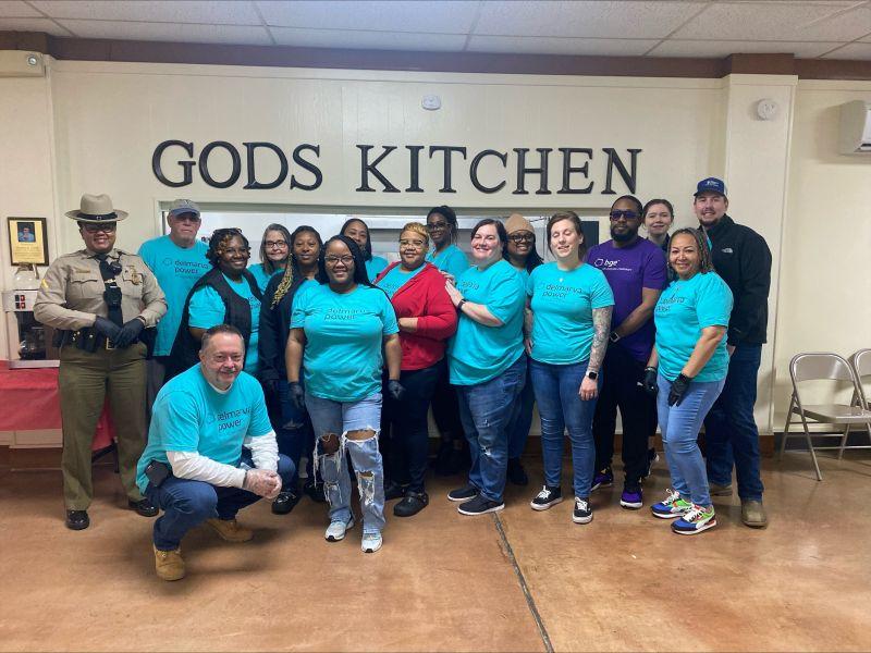 A group of volunteers posed in front of an indoor sign  "Gods Kitchen".